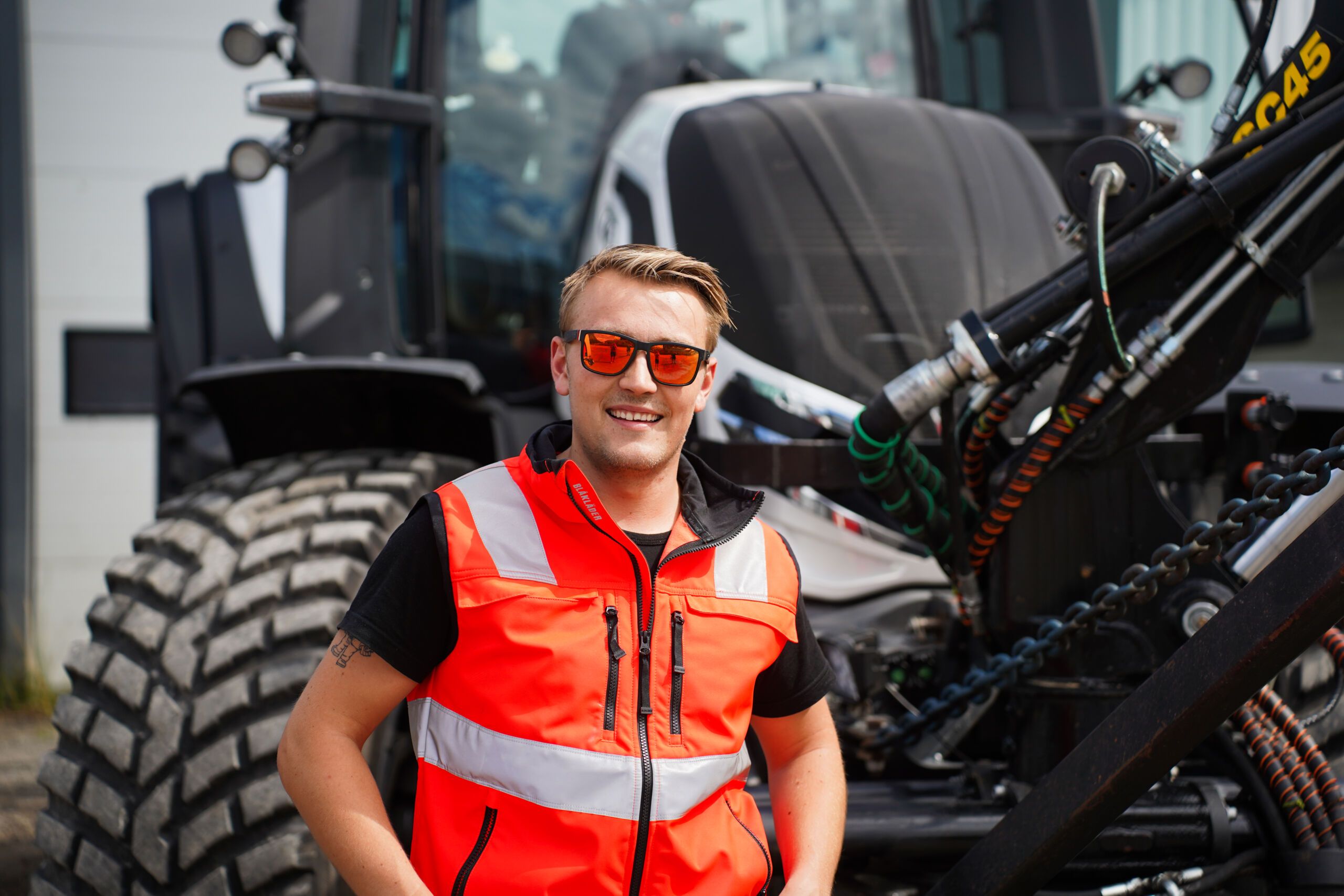 Elias Arviken i Elverum Anleggservice foran en av sine fire Valtra-traktorer, utstyrt med ekstra lys og personlig tilpasning. Bildet er tatt på en anleggsplass i Evlerum.